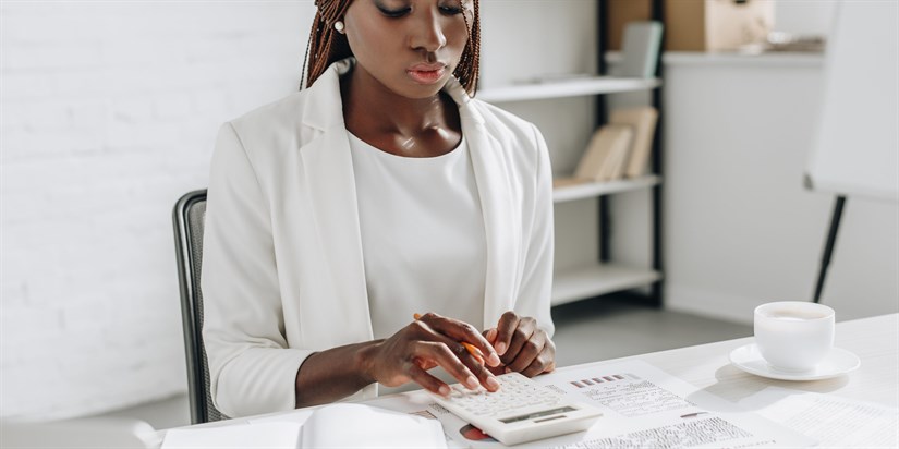 focused african american adult businesswoman in white formal wear working at office desk and using calculator